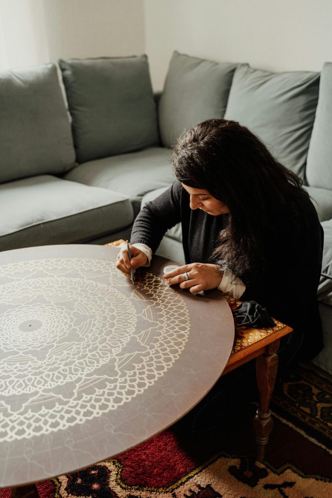 Creative woman intricately drawing a geometric mandala pattern on a wooden table indoors.